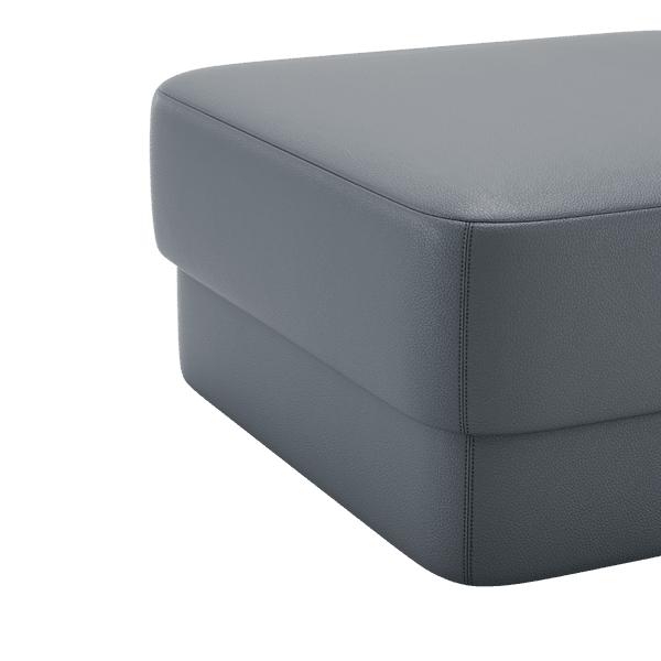 Een close-up van de Kate L Poef-ottoman benadrukt de grijze leren bekleding, de gladde textuur en de stiksels aan de boven- en zijkant, waardoor dit een elegant meubelstuk wordt.