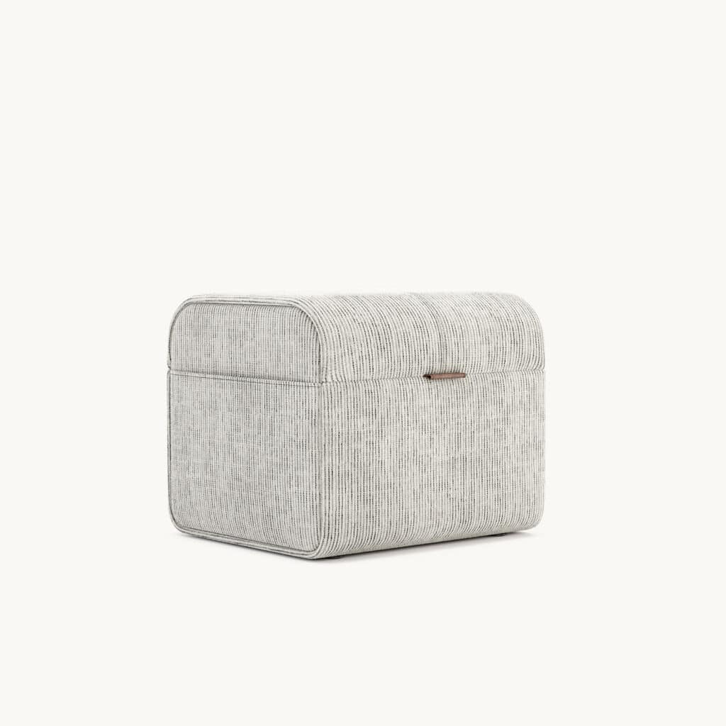 De Adley Poef S is een rechthoekige, stoffen opbergdoos met afgeronde randen, een subtiel gestreept design en een kleine handgreep aan de voorkant voor gemakkelijke toegang. Hij staat tegen een effen, lichte achtergrond.