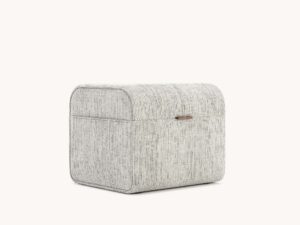 De Adley Poef S is een rechthoekige, stoffen opbergdoos met afgeronde randen, een subtiel gestreept design en een kleine handgreep aan de voorkant voor gemakkelijke toegang. Hij staat tegen een effen, lichte achtergrond.