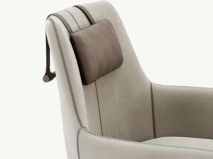 De Alexander Fauteuil is een moderne fauteuil met lichtbeige stof en een donkerbruine leren verstelbare hoofdsteun met banden. Het beschikt over strakke designelementen, waaronder zichtbare stiksels langs de naden, allemaal tegen een effen witte achtergrond om de verfijning te benadrukken.