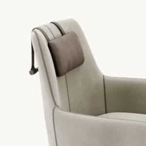 De Alexander Fauteuil is een moderne fauteuil met lichtbeige stof en een donkerbruine leren verstelbare hoofdsteun met banden. Het beschikt over strakke designelementen, waaronder zichtbare stiksels langs de naden, allemaal tegen een effen witte achtergrond om de verfijning te benadrukken.