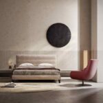Een minimalistische slaapkamer met een modern bed versierd met neutraal beddengoed, geaccentueerd door ronde zwarte wandkunst erboven. Rechts is er een levendige rode ELBA Fauteuil. De ruimte is gestyled in neutrale tinten en omvat een geweven rond kleed op de vloer.