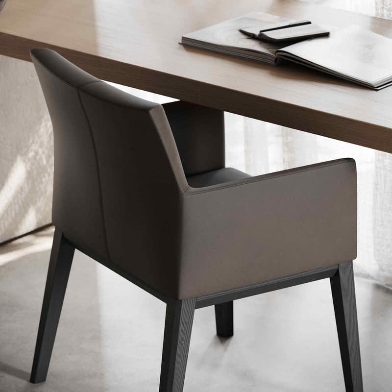 Een moderne Carter Stoel stoel met donkere houten poten staat naast een licht houten bureau. Op het bureau liggen een open boek, een gesloten notitieboekje en een pen, badend in zacht natuurlijk licht van een nabijgelegen raam.