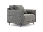 De Matthew Armstoel is een minimalistische, grijs gestoffeerde fauteuil met twee vierkante kussens, strakke zwarte metalen poten en een oppervlak van gestructureerde stof, afgezet tegen een effen witte achtergrond.