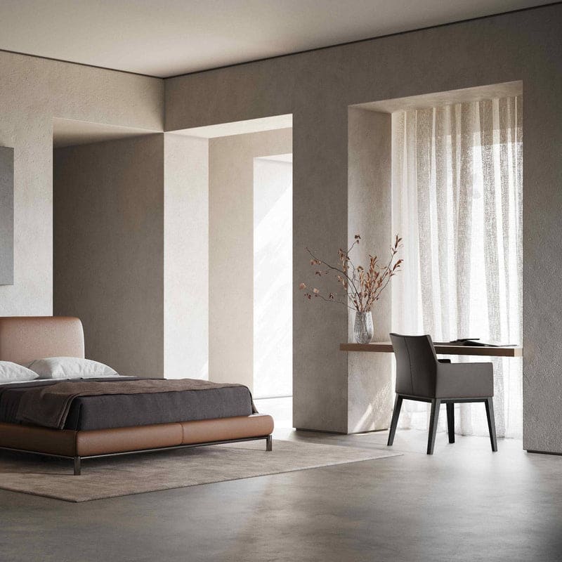 In een minimalistische slaapkamer met neutrale tinten, heeft het Carter Stoel bed een donker dekbed en lichte kussens. In de buurt, een houten bureau en stoel rusten bij een groot raam versierd met doorschijnende gordijnen. Een vaas met takken op het bureau introduceert een natuurlijk element.