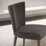 De Vianna Stoel, een elegant ontworpen donkergrijze gestoffeerde stoel met houten poten, verbetert de verfijning van een minimalistische kamer, omdat hij sierlijk op een stenen vloer staat. De hoge rugleuning draagt bij aan de eenvoudige maar stijlvolle uitstraling.