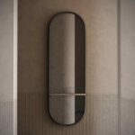 Een Cleo L Spiegel met een slank, donker frame siert een gestructureerde, neutraal gekleurde muur. Het onderste gedeelte contrasteert met het gladdere bovenste gedeelte. Deze spiegel reflecteert elegant de muur en subtiele verlichting, wat diepte toevoegt aan de ruimte.