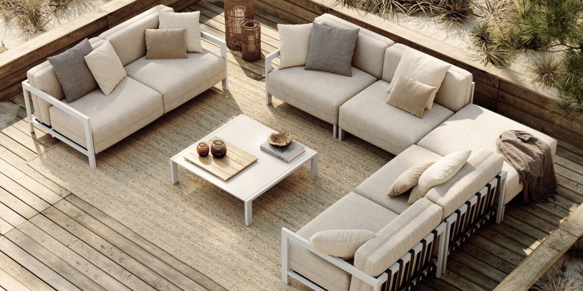 Luxe buitenmeubilair op een houten terras met comfortabele banken en sierkussens, ideaal voor ontspannen in de zomer.