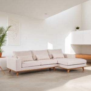 Een moderne woonkamer heeft een lichtbeige hoekbank met houten poten, op een lichtgrijze vloer. Een groene plant in een pot staat links en er hangt minimale kunst aan de muur. Witte kasten en een kleine plant staan op de achtergrond.