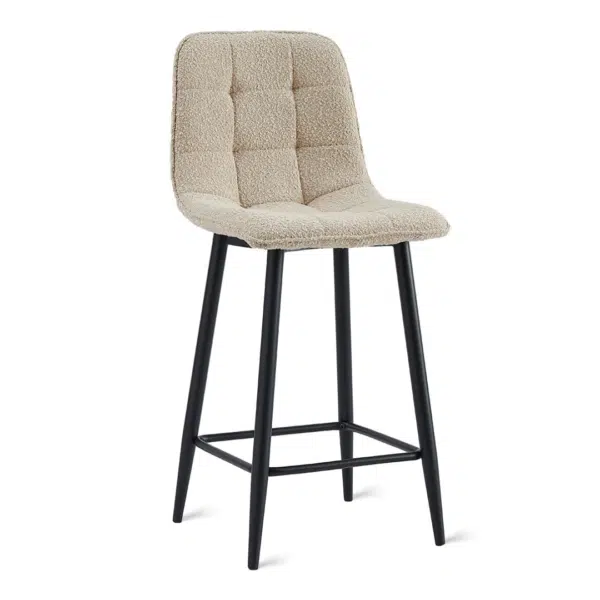 Beige gestoffeerde barkruk met een gecapitonneerde rugleuning en zwarte metalen poten. De kruk heeft een vierkante zitting, een gewatteerd oppervlak en een voetensteun die de poten verbindt voor extra ondersteuning.