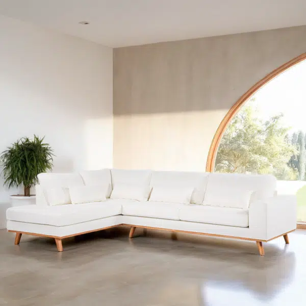 Een ruime woonkamer heeft een witte L-vormige sectionele bank met houten poten. De kamer heeft een gebogen, oversized raam dat natuurlijk licht binnenlaat en een potplant staat in de hoek. De vloer is van gepolijst beton.