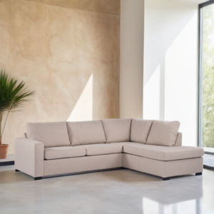 Een beige L-vormige bank staat in een moderne, lichte kamer met grote ramen. Een potplant in de hoek draagt bij aan het minimalistische decor. De muren zijn lichtgekleurd en complementeren de neutrale tinten van de bank.