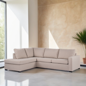 Een beige L-vormige bank met vijf kussens staat in een moderne, minimalistische kamer. De kamer heeft lichtgekleurde muren en een gepolijste betonnen vloer. Een groot raam laat natuurlijk licht binnen en er staat een potplant in de buurt.