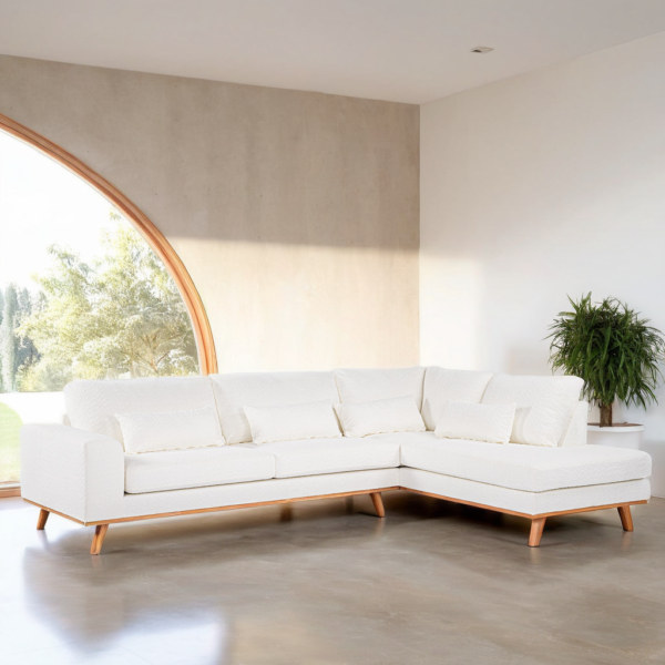 Een moderne woonkamer met een grote L-vormige witte bank met houten poten. Een potplant staat aan de rechterkant van de bank. Natuurlijk licht stroomt binnen via een groot, gebogen raam en verlicht de neutrale ruimte.