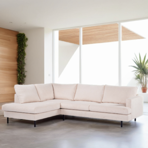 Een lichtbeige, L-vormige sectionele bank staat op een betonnen vloer in een moderne woonkamer. Grote ramen en een houten accentmuur met een verticale tuin bevinden zich op de achtergrond, waardoor er natuurlijk licht de ruimte vult. Een potplant is zichtbaar bij de ramen.