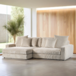 Een moderne woonkamer met een ruime driezitsbank van links naar rechts, gestoffeerd in de natuurlijke stof Lincoln 83 RIB920, diverse bijpassende kussens, een hoge groene plant, kamerhoge ramen met natuurlijk lichtinval en lichthouten lambrisering op één muur.