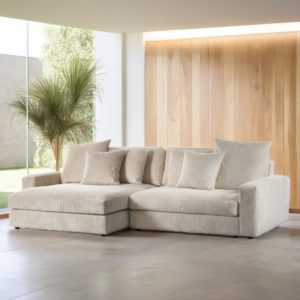 Een moderne woonkamer met een ruime driezitsbank van links naar rechts, gestoffeerd in de natuurlijke stof Lincoln 83 RIB920, diverse bijpassende kussens, een hoge groene plant, kamerhoge ramen met natuurlijk lichtinval en lichthouten lambrisering op één muur.