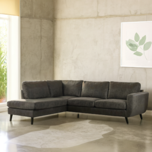 Moderne woonkamer met een groene 3-zits hoekbank (stof Yuma 39, S156), zwarte poten, betonnen muren, een groot zonnig raam en minimalistische bladkunstwerken aan de muur.