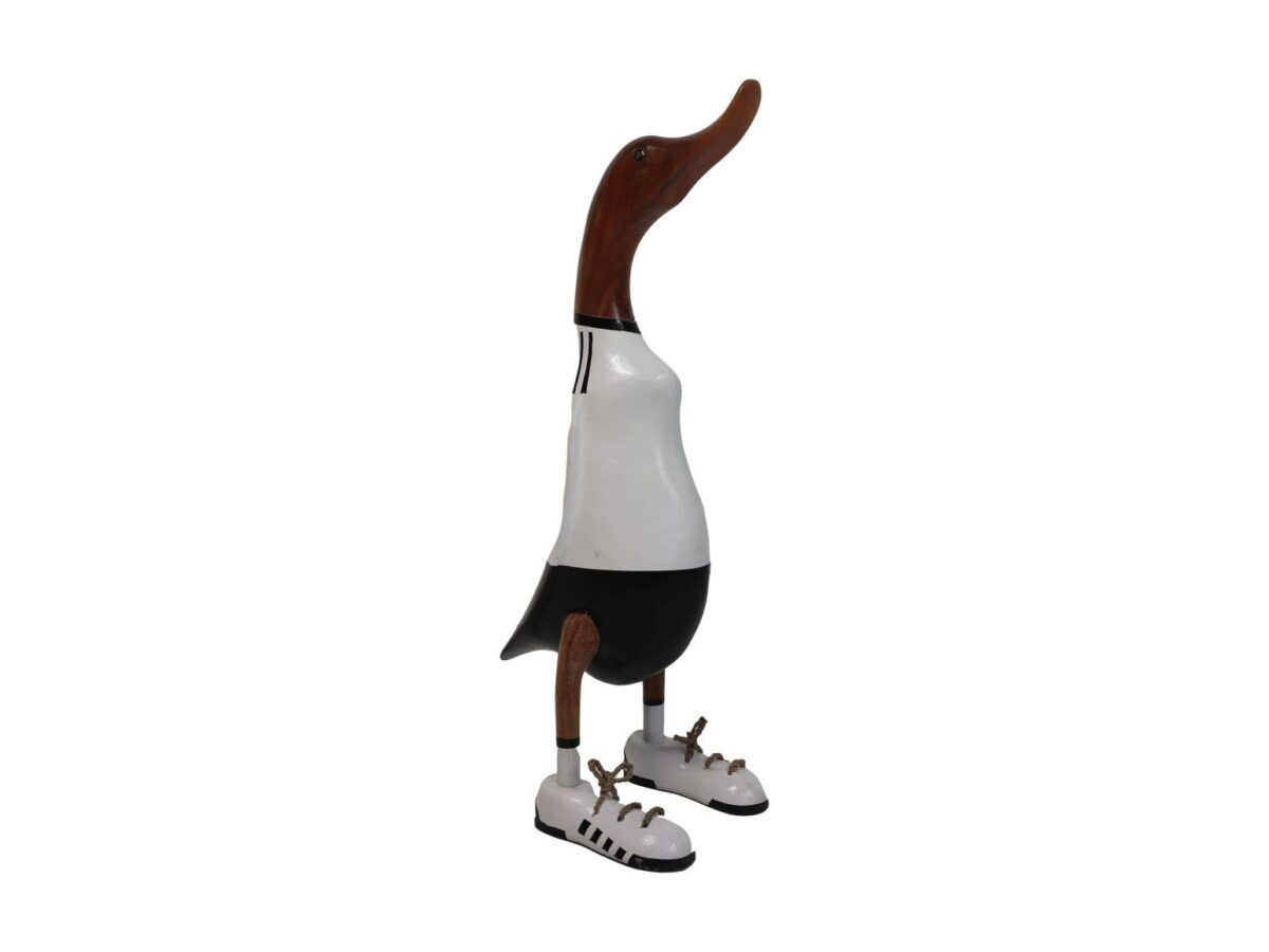 Houten eendensculptuur in een wit-zwarte outfit die lijkt op een sporttenue, met zwarte shorts en tennisschoenen. De snavel en kop zijn van natuurlijke houtkleur en de eend staat rechtop.