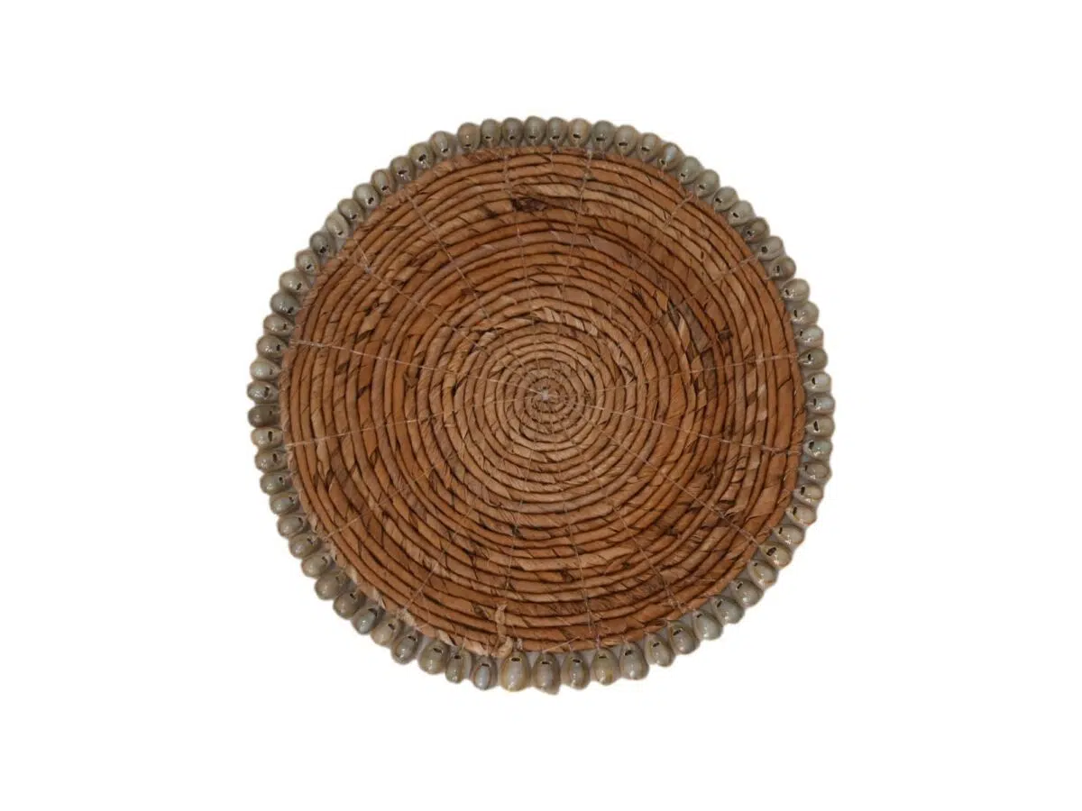 Een top-down view van een ronde gevlochten mand met een spiraalpatroon. De mand heeft een rand versierd met kleine schelpen rond de rand. De textuur oogt rustiek en natuurlijk.