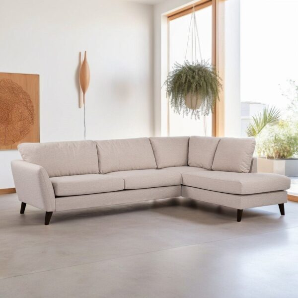 Een moderne woonkamer heeft een lichtbeige L-vormige sectionele bank met houten poten. Een hangplant staat voor een groot raam en een decoratief houten wandkunstwerk hangt aan de witte muur. De vloer is lichtgrijs.