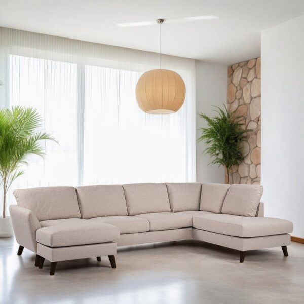 Een moderne woonkamer met een lichtgrijze L-vormige sectionele bank op een gladde vloer. Grote ramen met doorzichtige gordijnen laten natuurlijk licht binnen. Een ronde hanglamp en potplanten versterken het minimalistische decor. Een stenen accentmuur is gedeeltelijk zichtbaar.