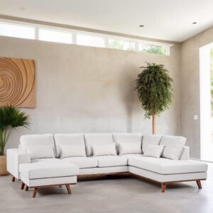 Een ruime woonkamer met een witte L-vormige sectionele bank tegen een lichtgrijze muur. De kamer heeft grote ramen, een rond houten wandkunstwerk en potplanten, wat een minimalistische en luchtige sfeer creëert.