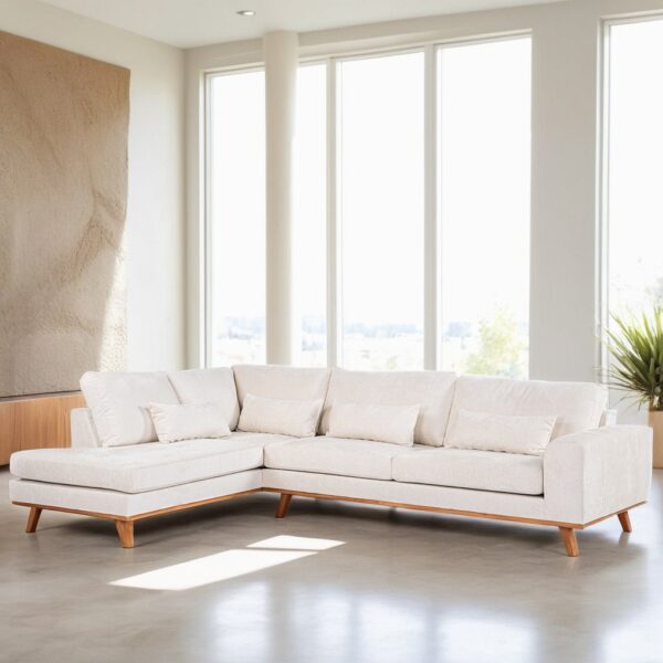 Een moderne woonkamer met een grote L-vormige crèmekleurige bank met lichte houten poten. De kamer heeft grote ramen, een muur met textuur en een potplant in de hoek. Natuurlijk licht vult de ruimte en benadrukt het strakke en minimalistische ontwerp.