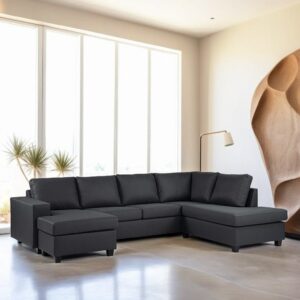 Een moderne woonkamer met een donkergrijze hoekbank met een voetenbank. Grote ramen zorgen voor natuurlijk licht en een hoge, minimalistische lamp staat rechts. De kamer heeft neutrale muren met een kunstwerk met textuur aan één kant.