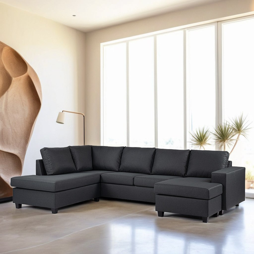 Een moderne woonkamer met een grote L-vormige donkergrijze bank. Zonlicht stroomt door de hoge ramen en benadrukt het minimalistische decor. Een strakke staande lamp staat naast de bank, met abstracte wandkunst en potplanten op de achtergrond.