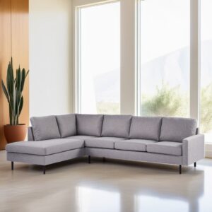 Een moderne woonkamer heeft een grijze L-vormige sectionele bank met zwarte poten tegen grote ramen. Een hoge cactus in een terracotta pot staat naast de bank en natuurlijk licht vult de ruimte, wat het minimalistische decor benadrukt.