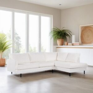 Een lichte woonkamer met een moderne witte sectionele bank op een lichte vloer. Grote ramen op de achtergrond laten natuurlijk licht binnen. Een potplant en abstracte kunst op het dressoir voegen groen en warmte toe aan de minimalistische ruimte.