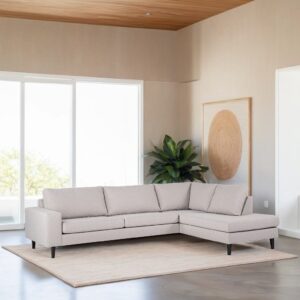 Een moderne woonkamer heeft een lichtgrijze L-vormige bank op een beige kleed. Grote ramen laten natuurlijk licht binnen. Een potplant staat in de hoek en een ingelijst abstract kunstwerk hangt aan de muur. Het plafond is van hout.