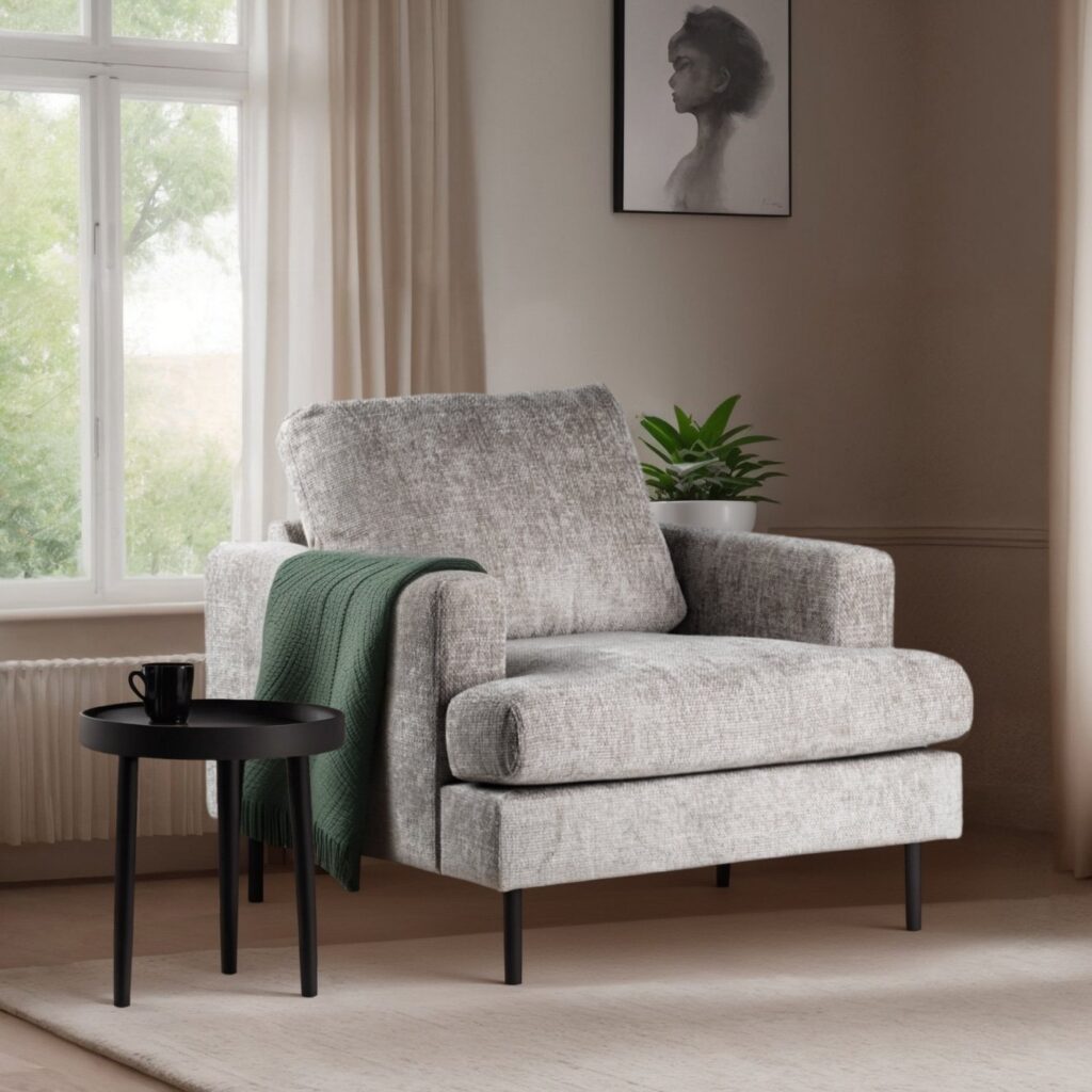 Een gezellige grijze fauteuil met een groene plaid over de zijkant, naast een kleine zwarte ronde tafel met een zwarte mok. Achter de stoel staat een potplant en een raam met doorzichtige gordijnen. Een portret hangt boven de stoel.