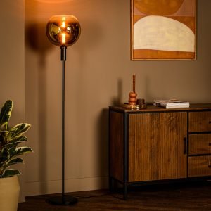 Een moderne woonkamer met een hoge staande lamp met een ronde amberkleurige glazen kap. Er staat een houten dressoir met boeken en decoratie, en ernaast staat een potplant. Er hangt een minimalistisch abstract schilderij aan de muur.