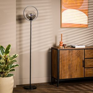Een moderne woonkamer met een strakke zwarte staande lamp, een houten dressoir en een potplant. De muur is beige met een geometrisch kunstwerk. Schaduwen met lamellen werpen zich over de scène.