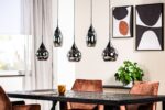 Moderne eetkamer met een donkere houten tafel, vier bruine gestoffeerde stoelen en vijf hangende hanglampen. Er staat een potplant op tafel. Abstracte kunst hangt aan de crèmekleurige muren en transparante gordijnen bedekken een raam.