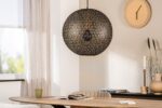 Een gezellige eetkamer met een grote, decoratieve hanglamp boven een houten tafel. De tafel heeft een open tijdschrift en een groene mok. Een ronde wandklok en lichte gordijnen sieren de minimalistische ruimte.