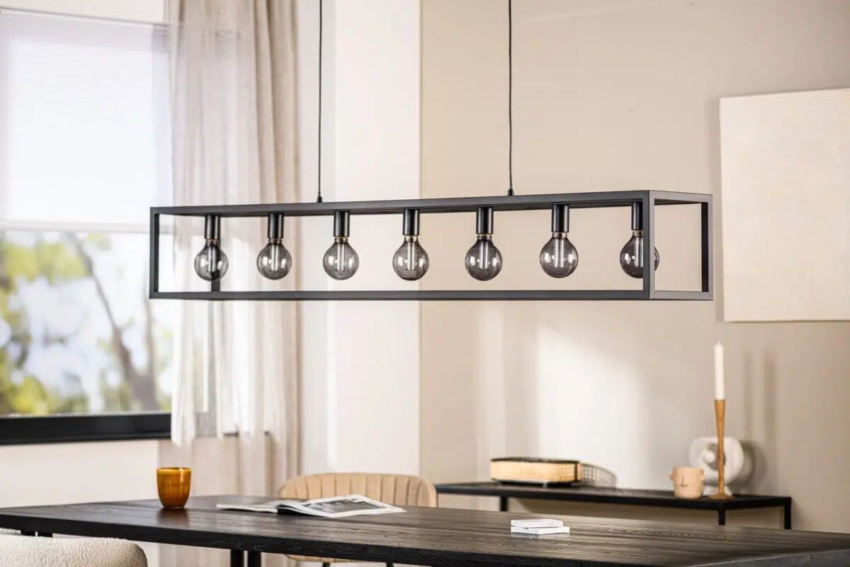 Een moderne eetkamer heeft een rechthoekige, zwarte metalen lamp met zeven zichtbare lampen. Eronder staat een donkere houten tafel met stoelen. Een raam met doorzichtige gordijnen, een kaars en minimale decoraties zijn op de achtergrond te zien.