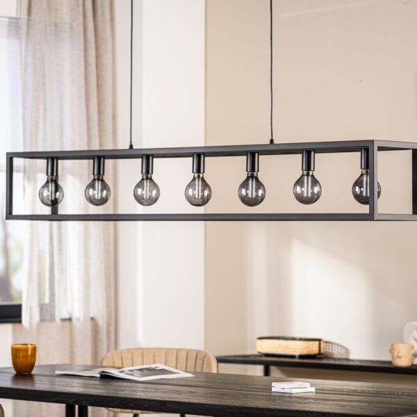 Een moderne eetkamer heeft een rechthoekige, zwarte metalen lamp met zeven zichtbare lampen. Eronder staat een donkere houten tafel met stoelen. Een raam met doorzichtige gordijnen, een kaars en minimale decoraties zijn op de achtergrond te zien.