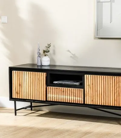 Een moderne zwarte mediaconsole met houten lattenkasten en open opbergruimte staat tegen een lichtgekleurde muur. Een kleine decoratieve vaas met groen en een vleugje zonlicht versterken het minimalistische decor.