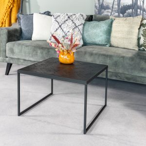 In een moderne woonkamer staat een groene bank met kleurrijke kussens, een gele deken over de armleuningen en op de lichtgrijze vloer staat de Bijzettafel Black Stack B340 zwarte salontafel met daarop een klein oranje vaasje met gedroogde bloemen.