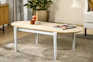 De Salontafel ovaal, 120x60 cm, B215 gouden pure salontafel met witte poten staat op een beige kleed en is versierd met een kaars, een vaasje en een tijdschrift. Een groene plant en neutrale meubels creëren een gezellige sfeer in de woonkamer.