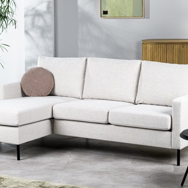Moderne woonkamer met de 3-zitsbank CL L+R in Valente V920 naturel, een rond bruin kussen, een zwarte ronde salontafel, een houten dressoir, een grote potplant en decoratie tegen een lichtgrijze muur.