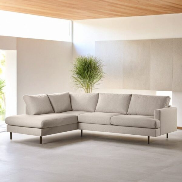 In de moderne woonkamer staat de beige L-vormige hoekbank met 3 zits hoek links, stof Bjorn 24, W460 op een lichte vloer, met een grote groene plant en natuurlijk licht dat door de hoge ramen op de achtergrond naar binnen stroomt.