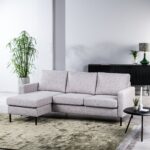 Moderne woonkamer met de 3-zitsbank CL L+R, stof Valente, V311 grijze hoekbank, groen vloerkleed, ronde zwarte bijzettafel met kleine plantjes, hoge potplant en zwart dressoir met decoratie tegen een witte muur.