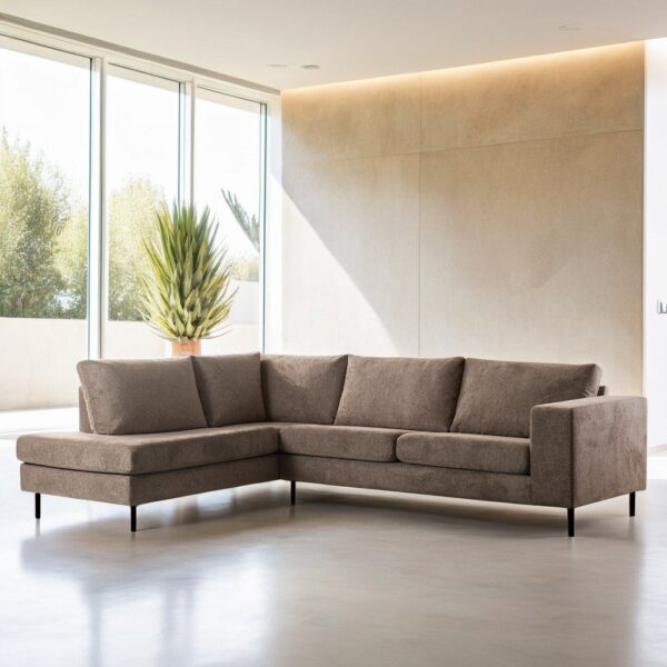 Een moderne taupekleurige driezits hoekbank (stof Lord 35, E520) staat in een lichte, minimalistische woonkamer met grote ramen, lichte muren en een potplant in de hoek.
