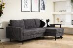 Moderne woonkamer met de 3-zitsbank CL L+R in RIB230 antraciet ribstof, een zwart-wit accentkussen, een lichte visgraatvloer, planten, drie ingelijste kunstwerken op een crèmekleurige muur en minimalistische decoratie op witte planken.