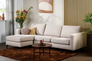 Moderne woonkamer met de 3-zitsbank CL L+R, stof Chloe, beige bank C460, ronde kussens, een klein houten salontafeltje op een bruin kleed, kleurrijke bloemen in een vaas, potplanten en abstracte kunst aan de muur.