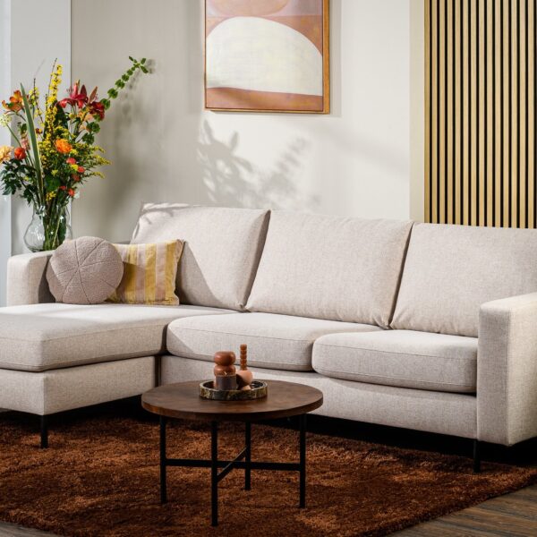 Moderne woonkamer met de 3-zitsbank CL L+R, stof Chloe, beige bank C460, ronde kussens, een klein houten salontafeltje op een bruin kleed, kleurrijke bloemen in een vaas, potplanten en abstracte kunst aan de muur.